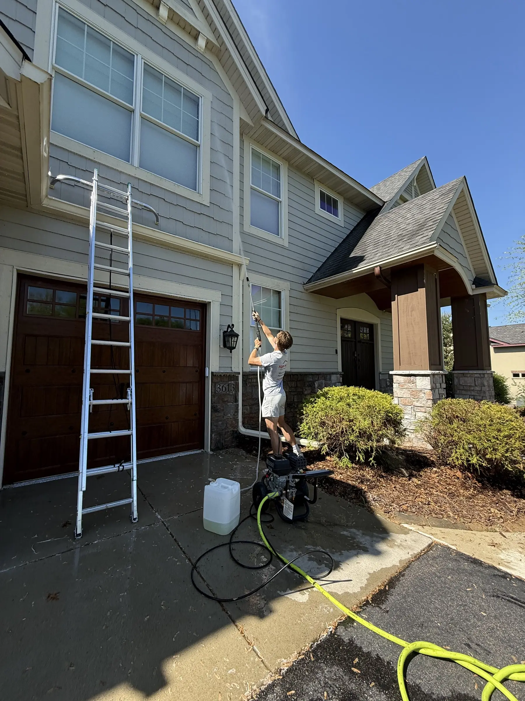 Pressure washing equipment set up on a wet driveway beside a home