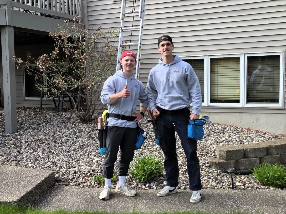 Sam and Reece, the founders of Top Haus Exteriors, standing in front of a home with their window cleaning gear
