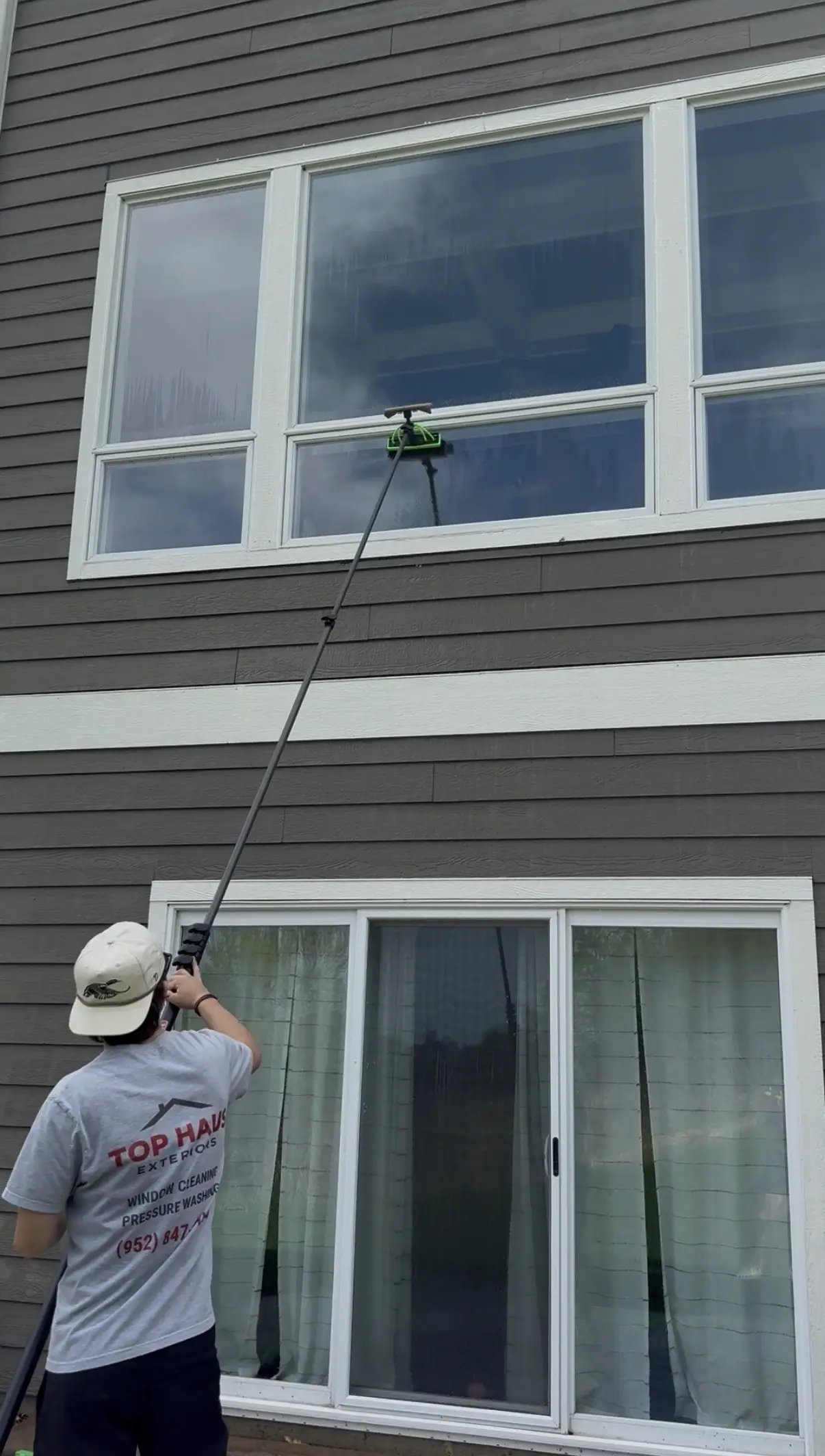 A Top Haus team member in a company shirt cleaning upper windows with a water-fed pole